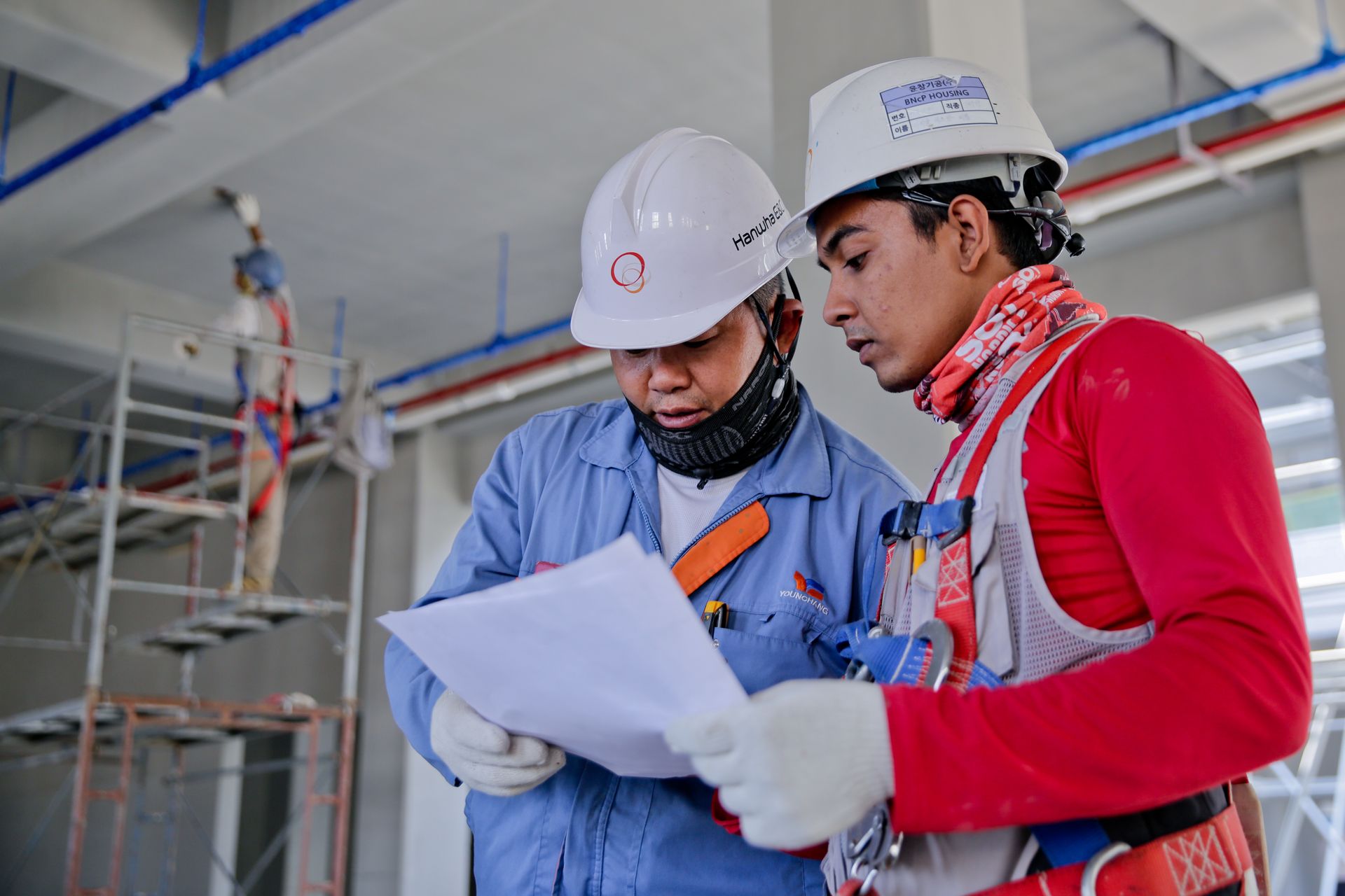 Two technicians in safety helmets reviewing a drawing on site